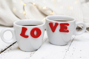 Boyalı ahşap bir yüzeyde üzerinde aşk yazan iki fincan kahve. Sevgililer günü, düğün günü, tarih