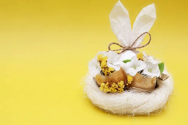 复活节构图：抽象的兔子蛋和金黄色背景的鸟巢中的花朵 — 图库照片