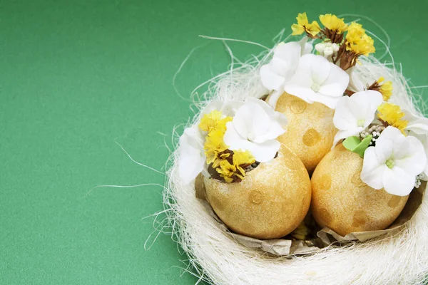 复活节构图：抽象的兔子蛋和金蛋，绿色背景的鸟巢里有花朵 — 图库照片