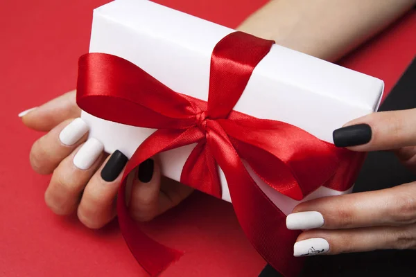 Caixa de presente com um arco nas mãos de uma mulher com manicure em um r — Fotografia de Stock