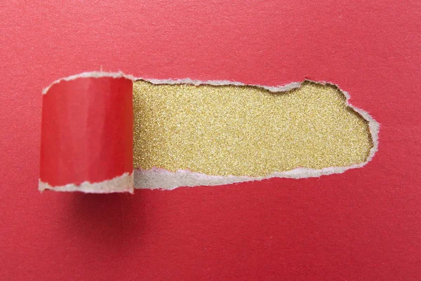 Hole in a sheet of red paper on a gold glitter background. Mock up with torn paper with space for text.