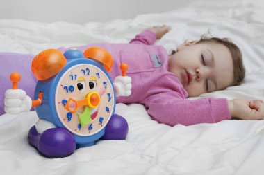 Uyuyan bir bebeğin arka planında neşeli bir çalar saat. Günlük rutin, sağlıklı bebek uyku konsepti.