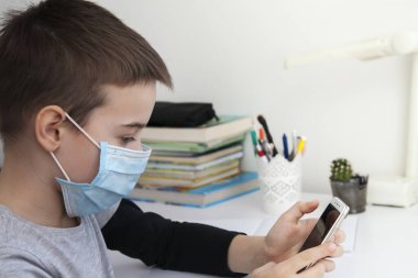 Evde eğitim gören bir çocuk elinde akıllı bir telefon ve tıbbi bir maskeyle. Coronavirus Karantina Konsepti