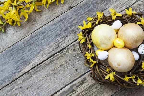 Nest with golden and yellow eggs with flowers on Wooden texture. Copy space for your Easter text