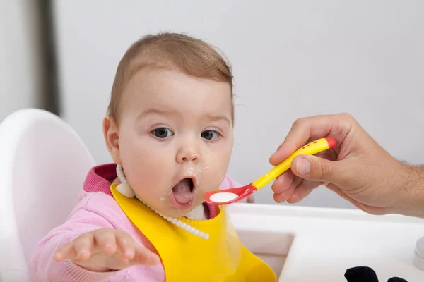 A baba etetés közben kinyitja a száját. Egy felnőtt keze szilikon kanállal eteti a babát. — Stock Fotó