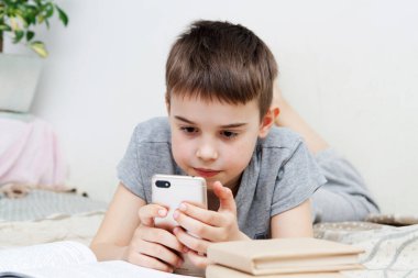 Elinde akıllı telefon olan bir çocuk yataktaki kitapların yanında ders veriyor. İnternet üzerinden uzaklık öğrenimi