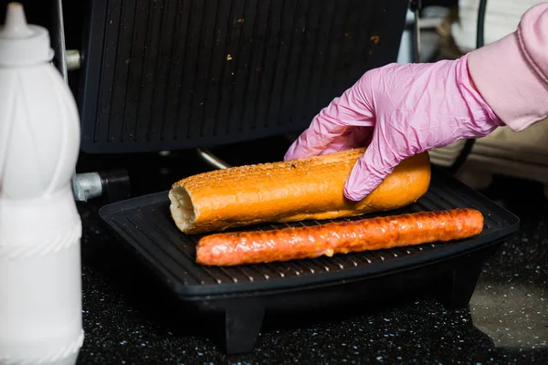 バーテンダーはソーセージとグリル面にロールでフランスのホットドッグを作る — ストック写真