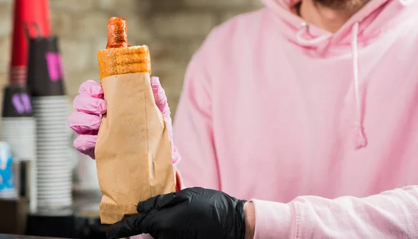 bartender holding french hot dog with grill sausage in paper package