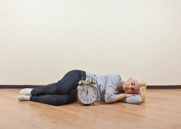 Девушка спит на полу в пустой комнате рядом с часами — стоковое фото