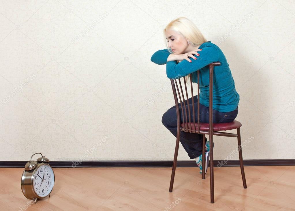 Sad girl sitting on a chair in an empty room and looks at his watch