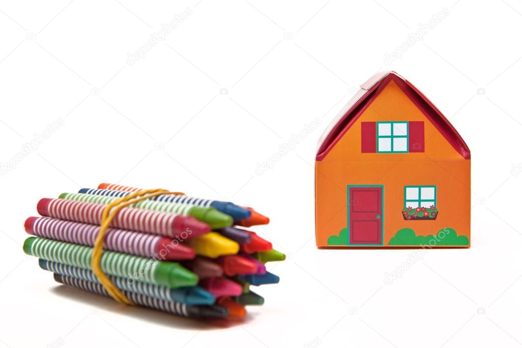 Kids folding paper house and wax crayons on white background.