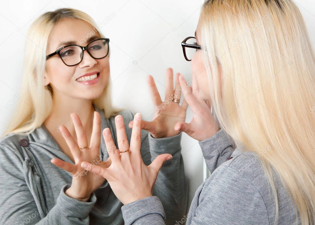 A happy emotional woman with glasses smiles at her reflection in the mirror.