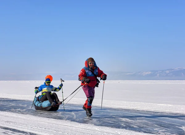 Bajkál-tó, Irkutsk régió, Oroszország - 2017. március 08.: Ember a korcsolyát tekercs lány húzza szánkó — Stock Fotó