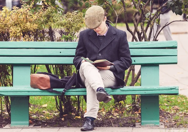 Ung man sitter på bänken och läser en bok — Stockfoto