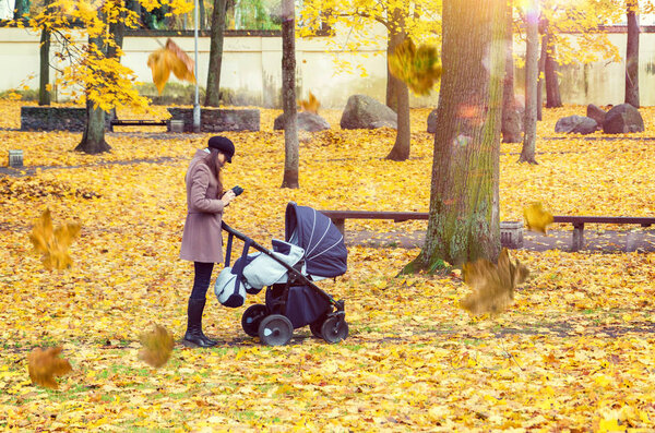 Young mother with baby pram in autumn park 