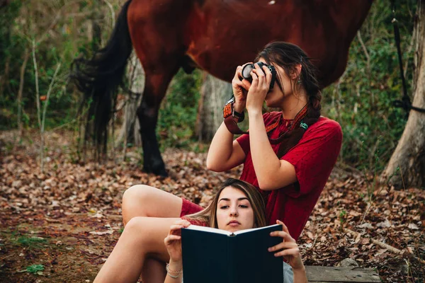 Jovens mulheres lendo um livro e tirando fotos na floresta — Fotografia de Stock