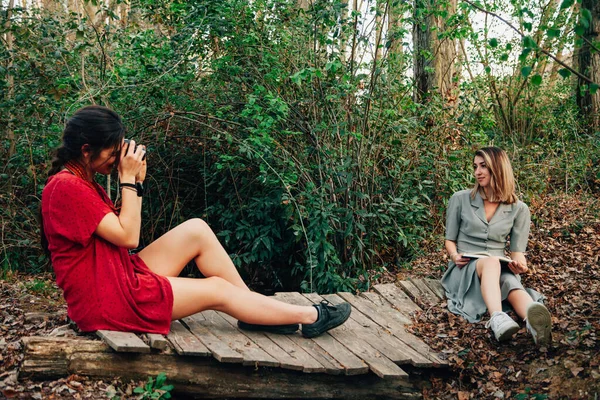 Jovens mulheres lendo um livro e tirando fotos na floresta — Fotografia de Stock