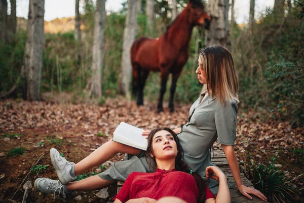 Jovens mulheres lendo um livro e tirando fotos na floresta — Fotografia de Stock