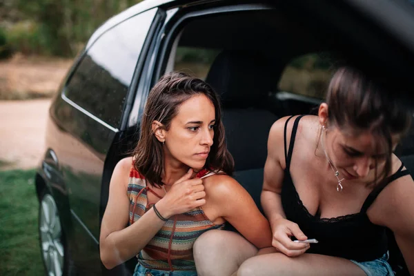 Dos jóvenes lesbianas enrollando un cigarrillo hecho a mano en el coche — Foto de Stock