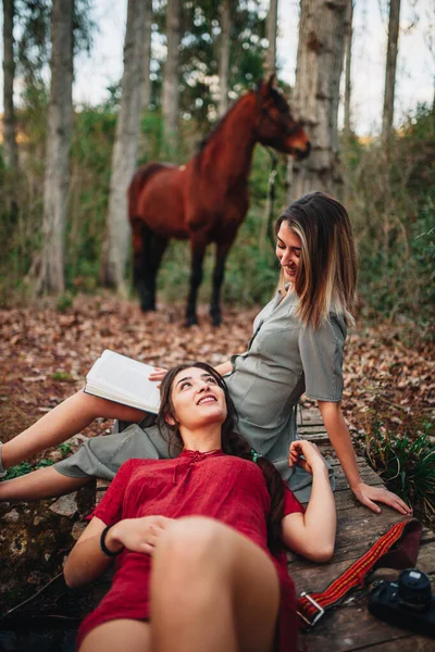 Mujeres jóvenes leyendo un libro y tomando fotos en el bosque — Foto de Stock