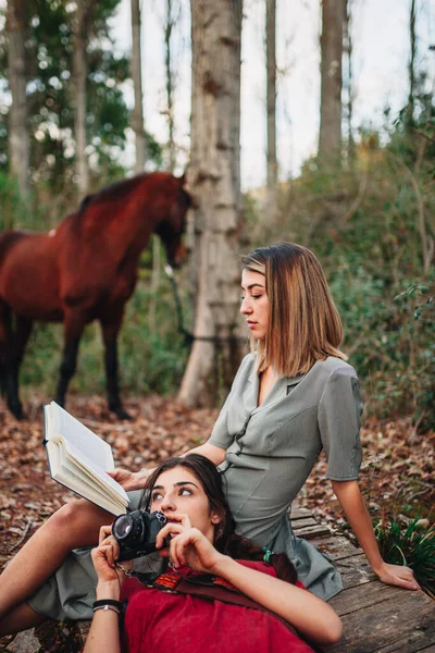 Молодые женщины читают книгу и фотографируют в лесу — стоковое фото