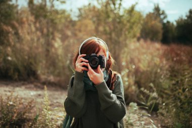 Genç bir kadın ormanda eski bir kamerayla fotoğraf çekiyor.