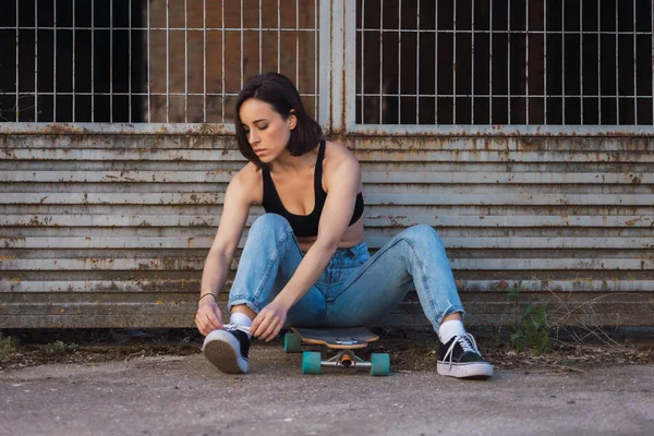 Jeune femme assise sur son patin dans une vieille rue industrielle — Photo