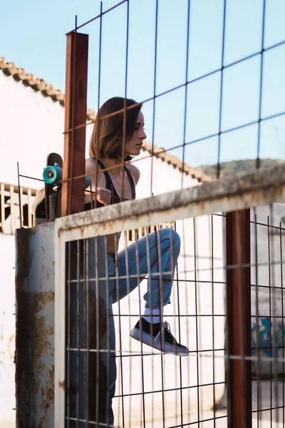 Νεαρή γυναίκα σκέιτερ προσπαθεί να σκαρφαλώσει πάνω από το φράχτη — Φωτογραφία Αρχείου