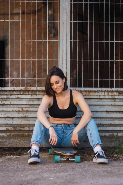 Mujer joven sentada en su patín en una vieja calle industrial —  Fotos de Stock