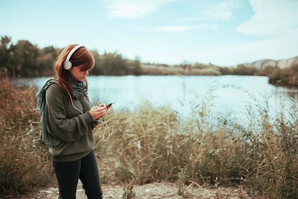 Jeune femme utilisant son smartphone près d'un lac avec écouteurs — Photo