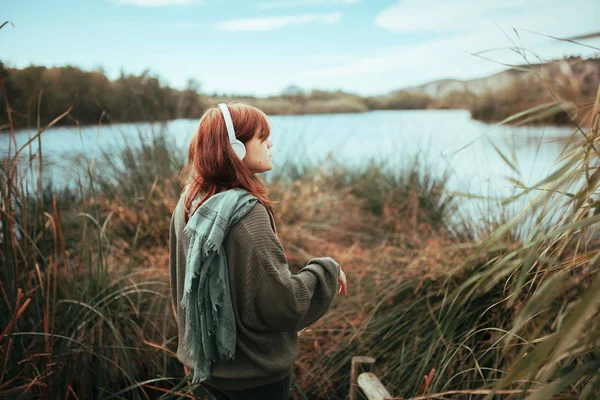 Jonge vrouw met behulp van haar smartphone in de buurt van een meer met hoofdtelefoon — Stockfoto