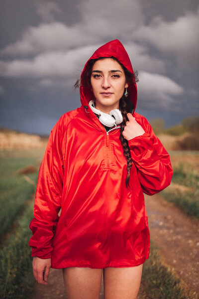 Young woman standing with raincoat and headphones on the field — Stock Photo, Image