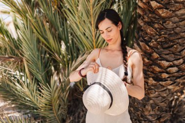 Çölde palmiye ağacına yakın duran elbise giymiş bir kadın.