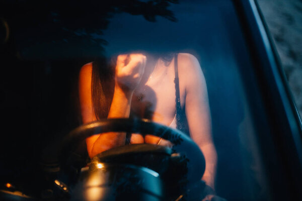 Young woman puts on makeup inside a car at sunset