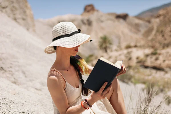 Mulher lendo um livro vestindo vestido assentos no deserto — Fotografia de Stock