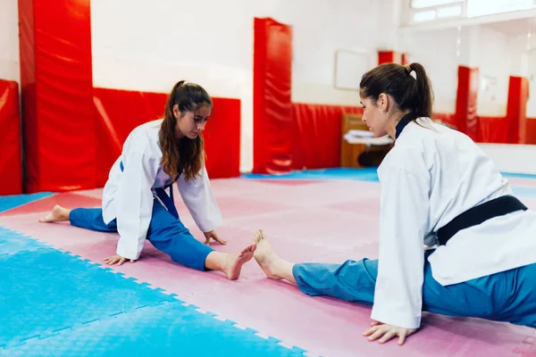Young woman stretching in a dojo wearing taekwondo suits — Stock Photo, Image