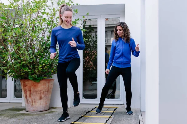 Two young women doing agility ladder exercise on a terrace