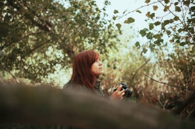 Ormanda eski bir analog kamerayla fotoğraf çeken genç bir kadın.