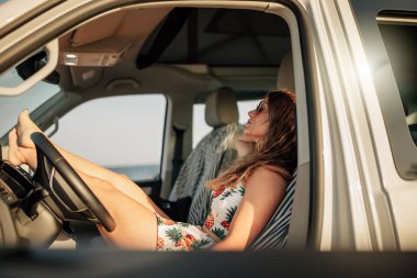 Şoför koltuğunda oturan genç bir kadın. Minibüste, mini elbiseli.