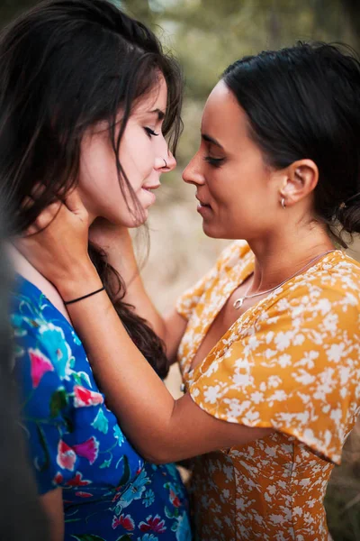 Two women kissing in the woods with dresses