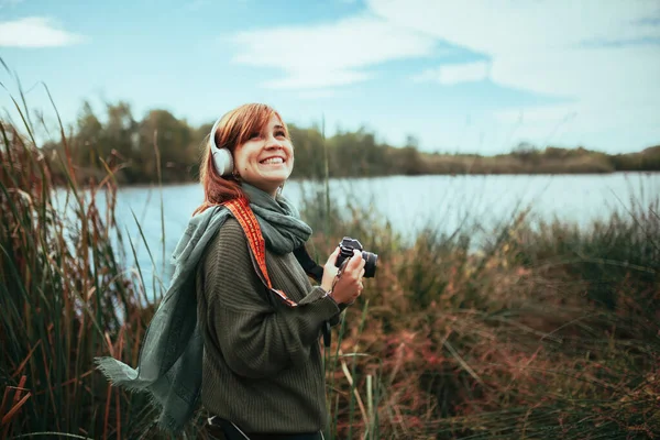 年轻女子拿着老式模拟相机和耳机在森林里拍照 — 图库照片