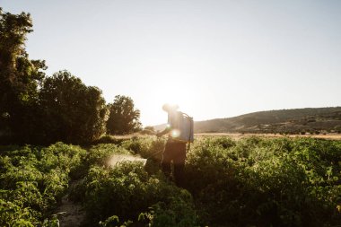 Genç çiftçi organik gübreyi manuel pompa tankıyla püskürtüyor. Eski bir şapka ve ekose gömlek giyiyor.