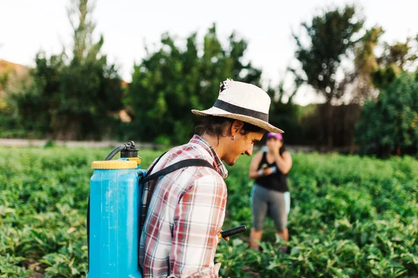 年轻农民穿着旧帽子和格子花衬衫 用手动水泵罐喷洒有机肥 — 图库照片