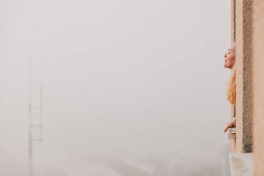 Kadın pencereden dışarı bakıyor ve nefes alıyor.