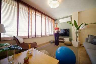 Kadın pencerenin önünde yoga yapıyor.