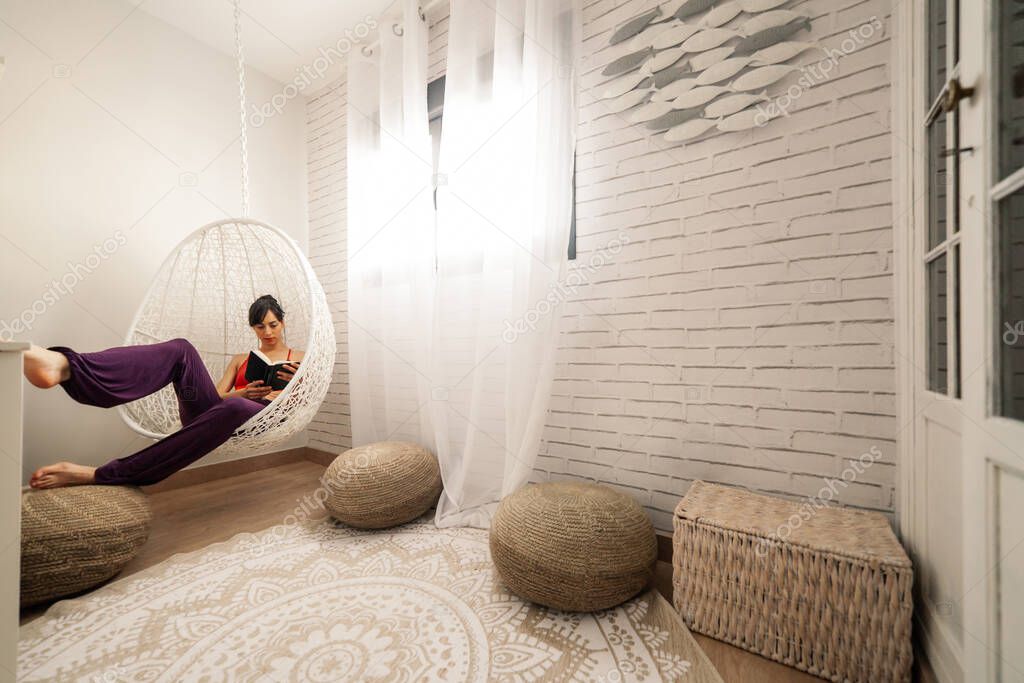 Woman reading a book in a hammock in her bedroom