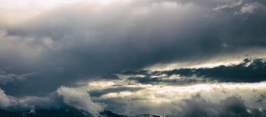 Mavi gökyüzü ve ağır bulutlar dağ silsilesi.