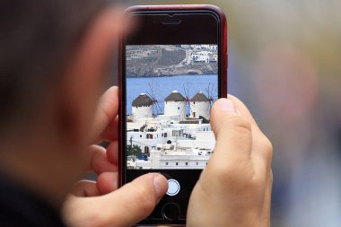 Mykonos Adası belirene tablet, smartphone adamın elinde. Arka plan bulanık