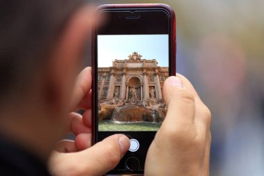 Tablet, adamın elinde smartphone Fontana di Trevi Roma resmi görünür. Arka plan bulanık