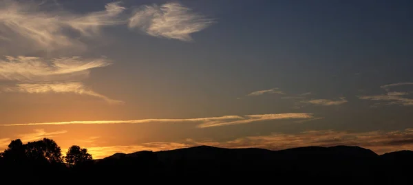 Puesta de sol sobre colinas silueta, nubes dispersas en el cielo. El atardecer está en el lado izquierdo . —  Fotos de Stock